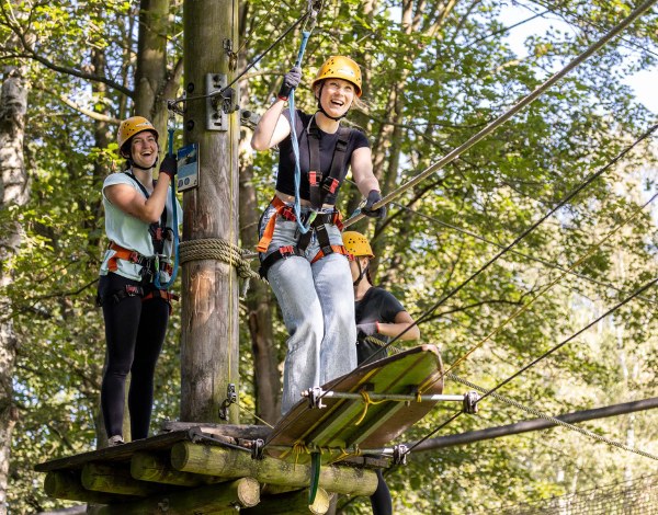 Zwei lachende Jugendliche bereiten sich vor sich nacheinander ber eine Seilbahn mit rollender Plattform zu ziehen